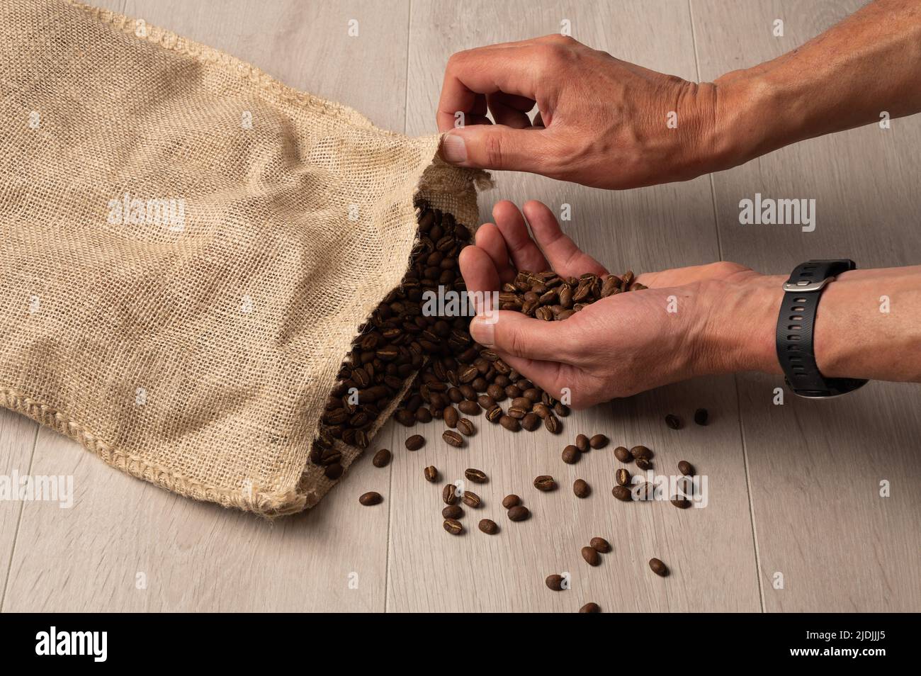 Kaffeebohnen, die in der Hand liegen, werden aus einer hessischen Tasche auf hellem Holzhintergrund aus nächster Nähe verschüttet Stockfoto