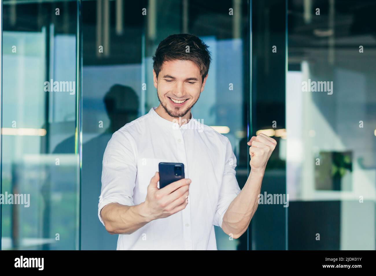 Glücklicher Geschäftsmann, der auf den Smartphone-Bildschirm schaut und den Gewinner so zum Lächeln und Lachen macht. Die guten Nachrichten lesen, Erfolge feiern, Erfolg haben Stockfoto