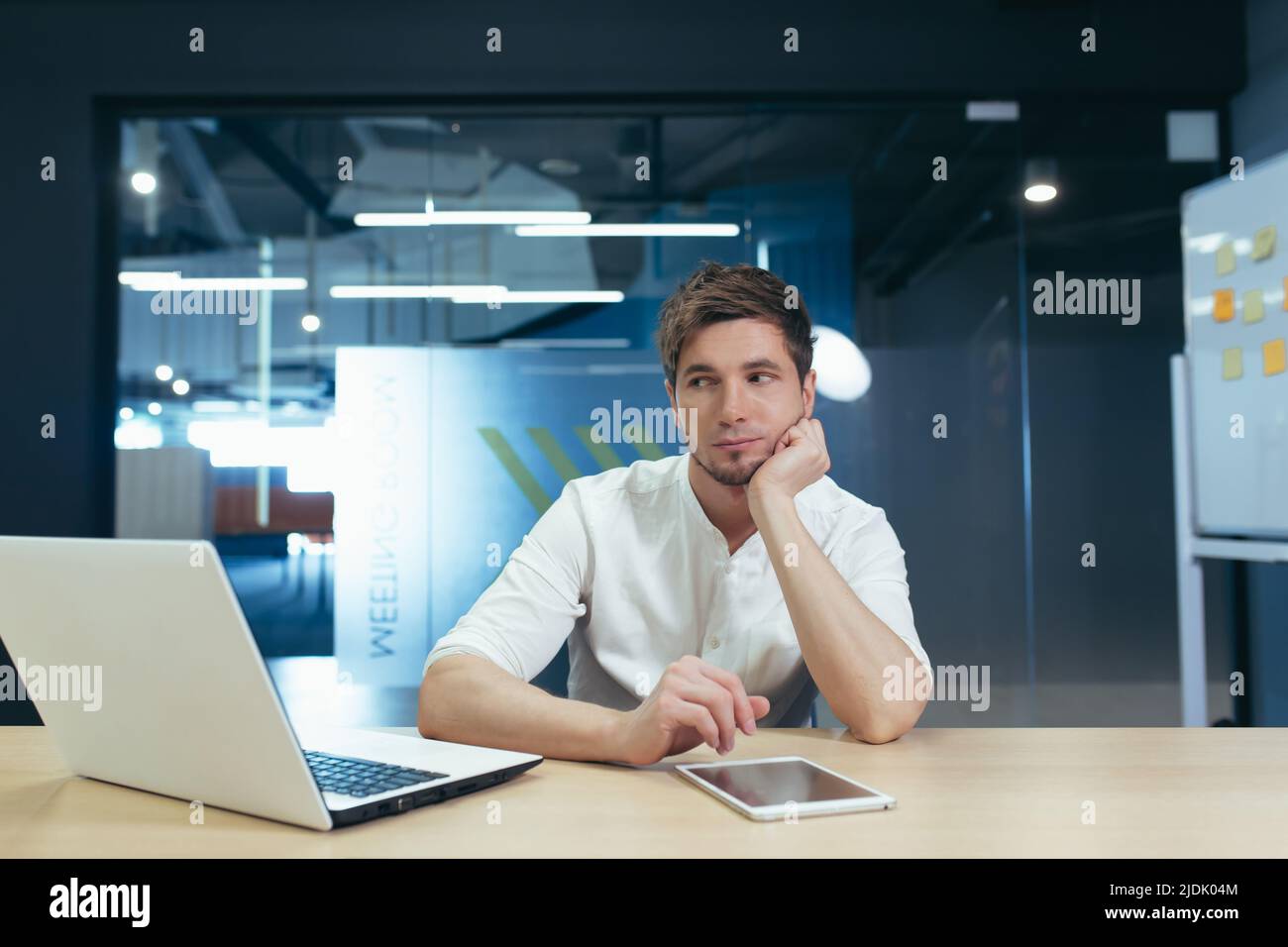 Langweiliger Arbeitstag. Porträt eines jungen Mannes, der traurig im Büro am Schreibtisch sitzt und seinen Kopf in der Hand hält. Er mag seinen Job nicht. Müde Stockfoto