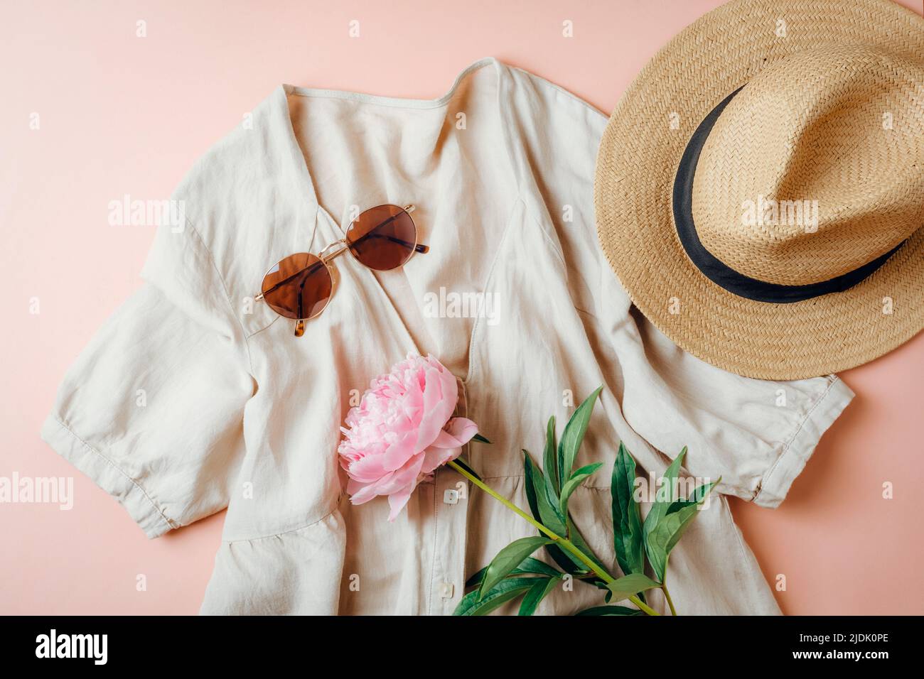 Sommerlicher Casual-Style. Stilvolle Frauenkleidung und Accessoires. Leinenkleid, Sonnenbrille, Hut und Pfingstrose auf rosa Hintergrund. Flach liegend, Draufsicht. Stockfoto