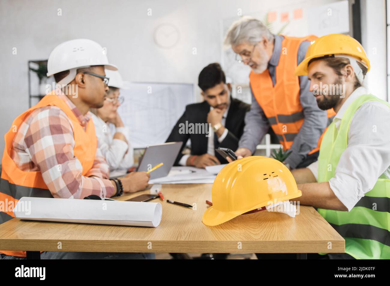 Konzentrieren Sie sich auf schützenden Hardhut. Kompetente Ingenieure, Designer und Architekten leiten die Arbeitskonferenz im Bürozentrum. Gruppe multikultureller Menschen, die Anzug, Uniform und Schutzhelm tragen. Stockfoto