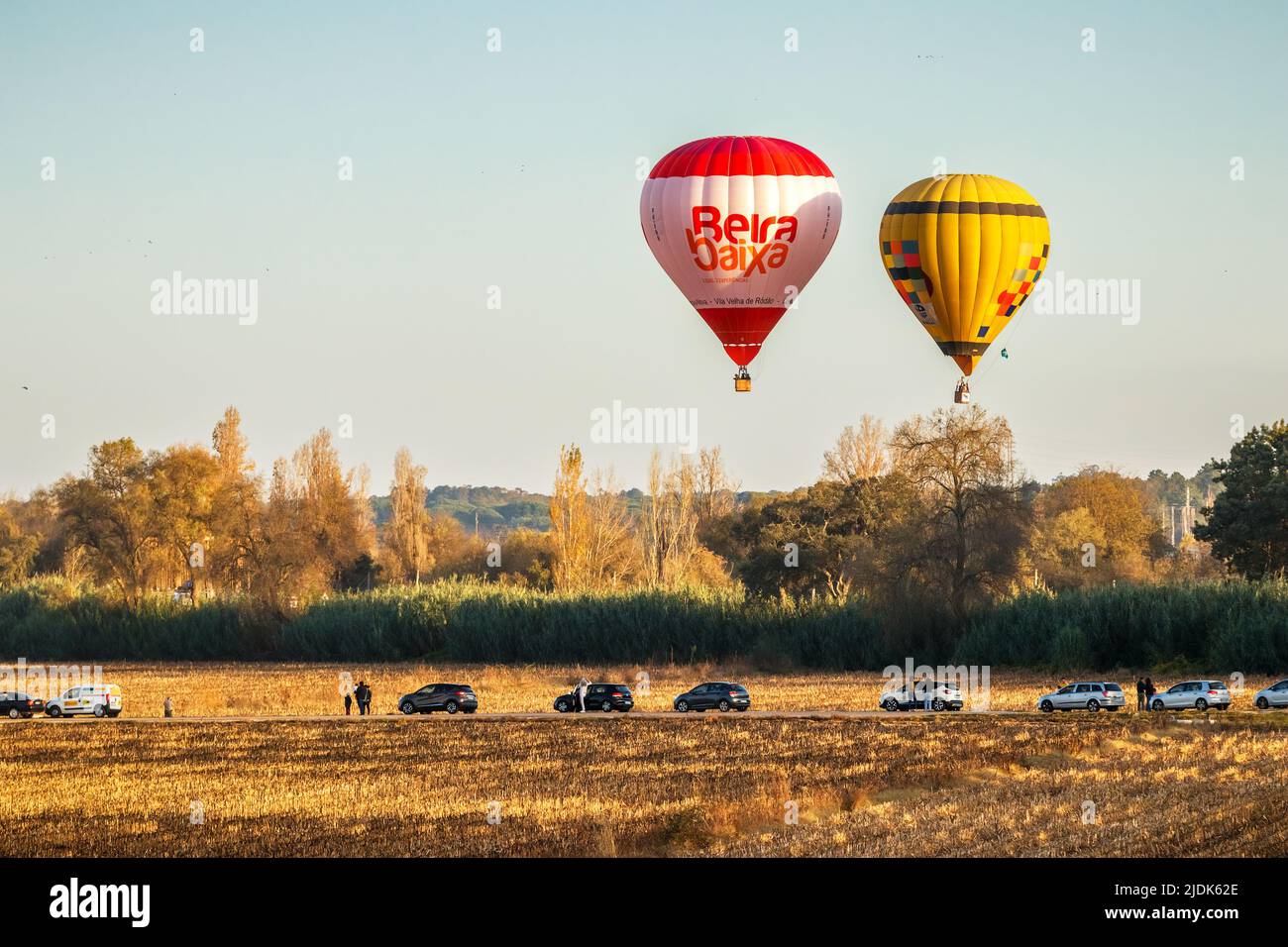 Coruche, Portugal - 13. November 2021: Zwei Heißluftballons fliegen über Bäume und Ackerland in Coruche, Portugal, mit geparkten Autos und Menschen beobachten Stockfoto