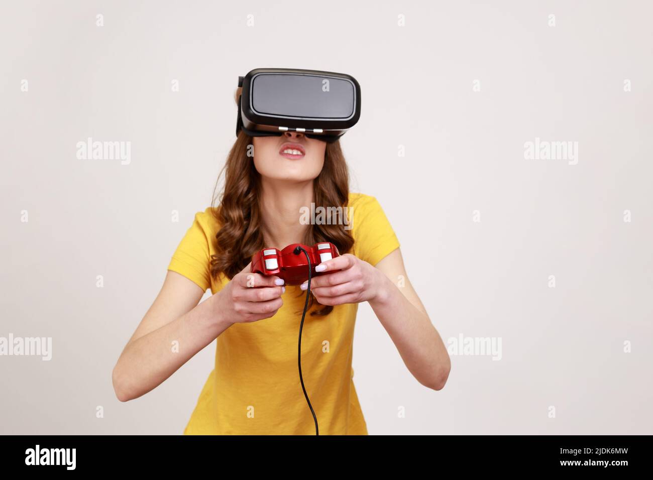 Konzentrierte Frau im jungen Alter in VR-Brille und beobachten virtuelle Welt mit erstaunt schockiert Ausdruck, Videospiel mit Joystick spielen. Innenaufnahme des Studios isoliert auf grauem Hintergrund. Stockfoto