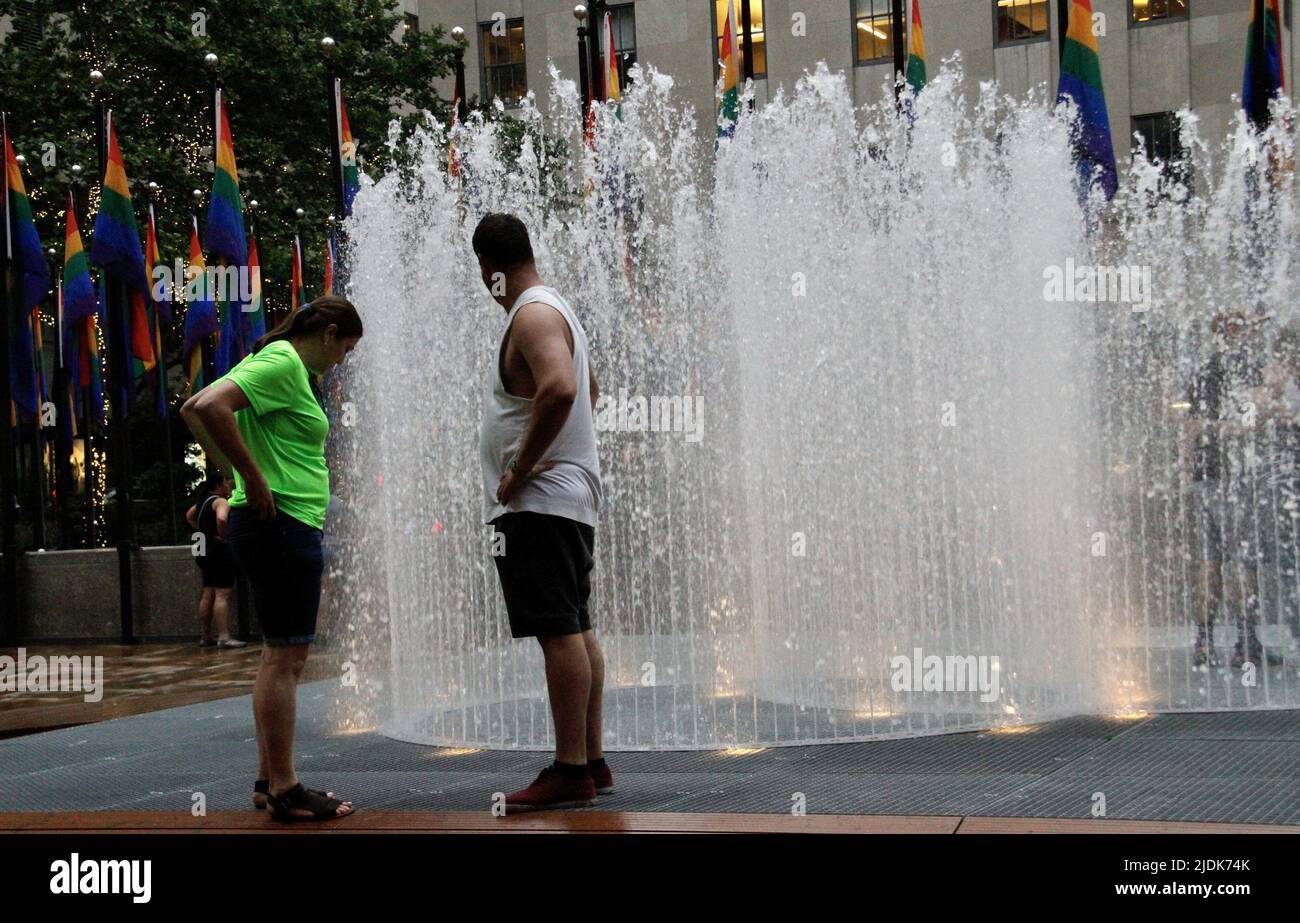 21. Juni 2022, New York, USA: (NEUE) Wasserbrunnen im Rockefeller Center. 21. Juni 2022, New York, USA : der Water Fountains Place im Rockefeller Center direkt vor der Eislaufbahn zieht am ersten Sommertag New Yorker und Touristen an. Die Leute kommen in die Brunnen und werden donÃ¢â‚¬â„¢nicht nass. Das Wasser kommt aus dem Boden und umgibt die Innenseite, ohne sie nass zu machen, und itÃ¢â‚¬â„¢ist eine Quelle von Attraktionen thatÃ¢â‚¬â„¢s mehr Menschen in die Mitte ziehen und abgesehen von den Stolz Flaggen überall auf der Eisbahn zum Gedenken an Pride Month in New York. (Credit Ima Stockfoto