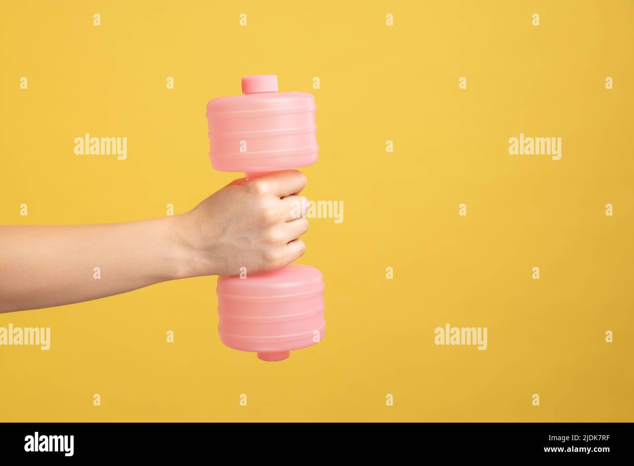 Nahaufnahme der Frau Hand hält rosa Hantel , Geräte für zu Hause Workout, Fitness und Aktivität, Sport und gesunde Lebensweise Konzept. Innenaufnahme des Studios isoliert auf gelbem Hintergrund. Stockfoto
