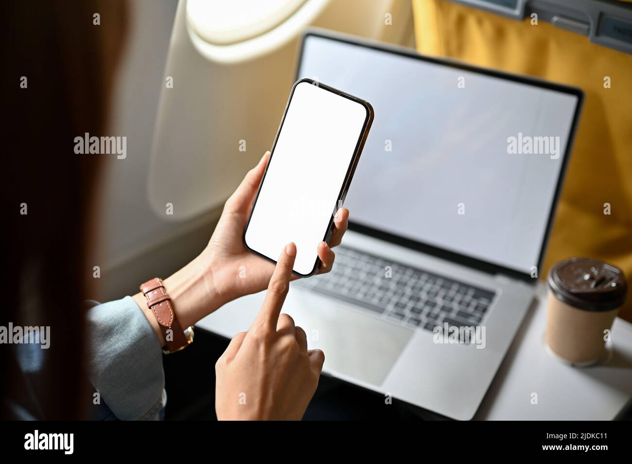 Nahaufnahme, weibliche Reisende mit einem Smartphone und einem tragbaren Laptop im Flugzeug. Modell mit weißem Bildschirm für Telefon und Laptop. Stockfoto
