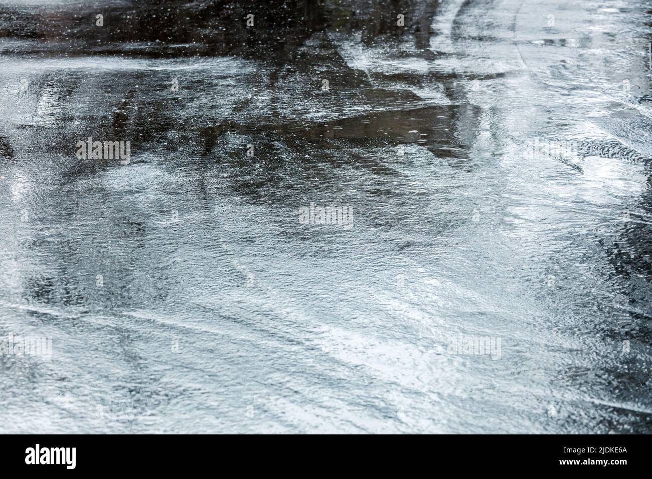 Dunkler nasser Asphalt bei Regen. Straßenbelag mit Pfützen und Regentropfen. Stockfoto