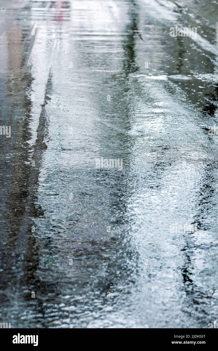 Nasse Asphaltstraße nach Regen mit Reflexen des Himmels. Regnerisches Wetter in der Stadt. Stockfoto