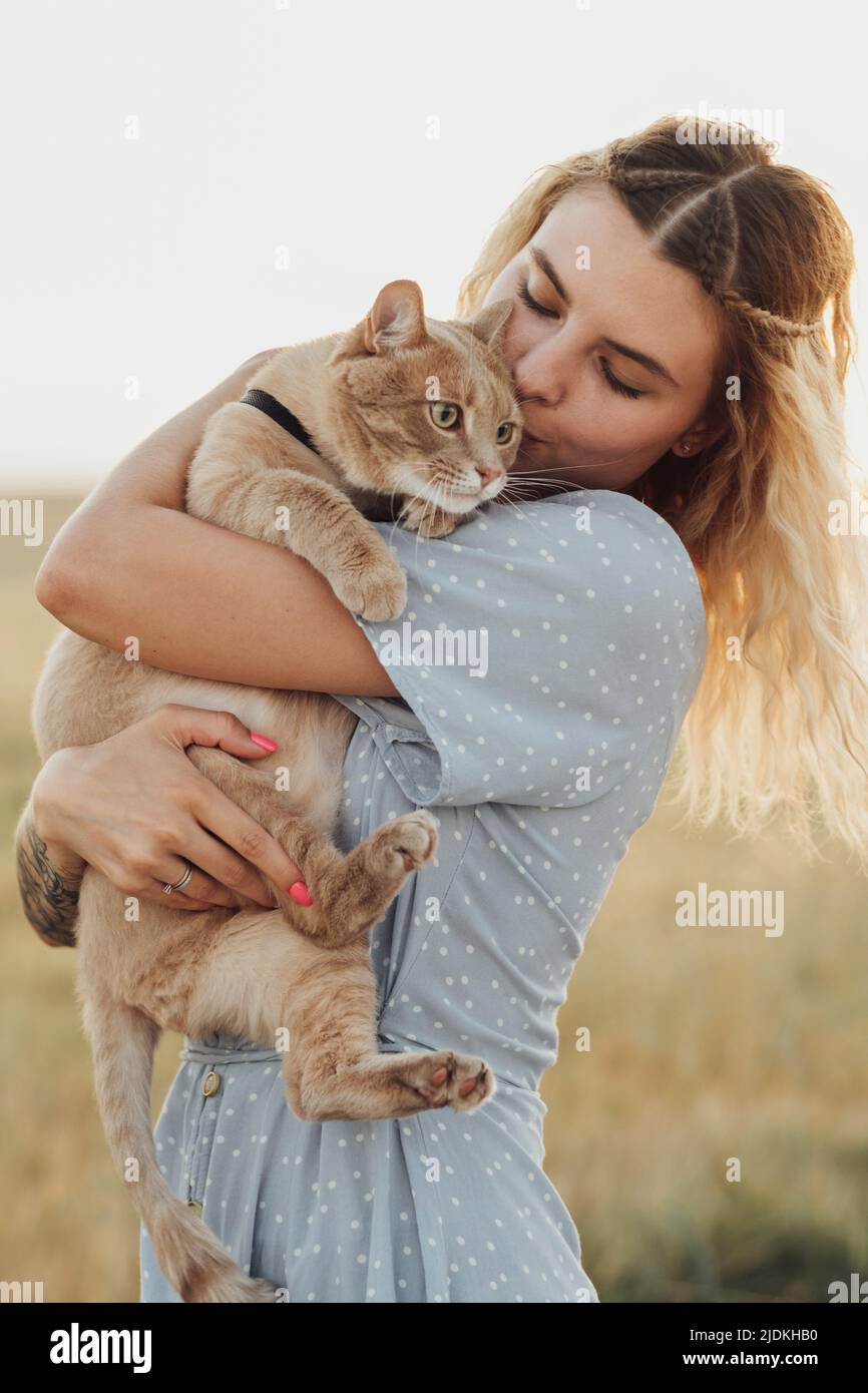 Kaukasische junge Frau in blauem Kleid gekleidet hält ihre rote Katze im Freien bei Sonnenuntergang Stockfoto