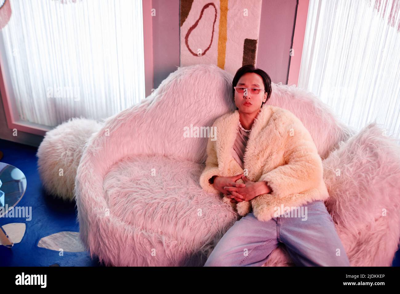 Porträt eines asiatischen jungen Mannes in Pelzmantel und Party-Outfit entspannen in clu Lounge von rosa Neonlicht beleuchtet Stockfoto