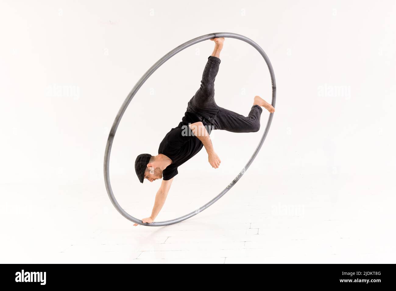 Ganzer Körper des aktiven Barfuß-akrobaten, der einen Arm Münzstunt mit cyr-Rad vor weißem Hintergrund im hellen Studio durchführt Stockfoto