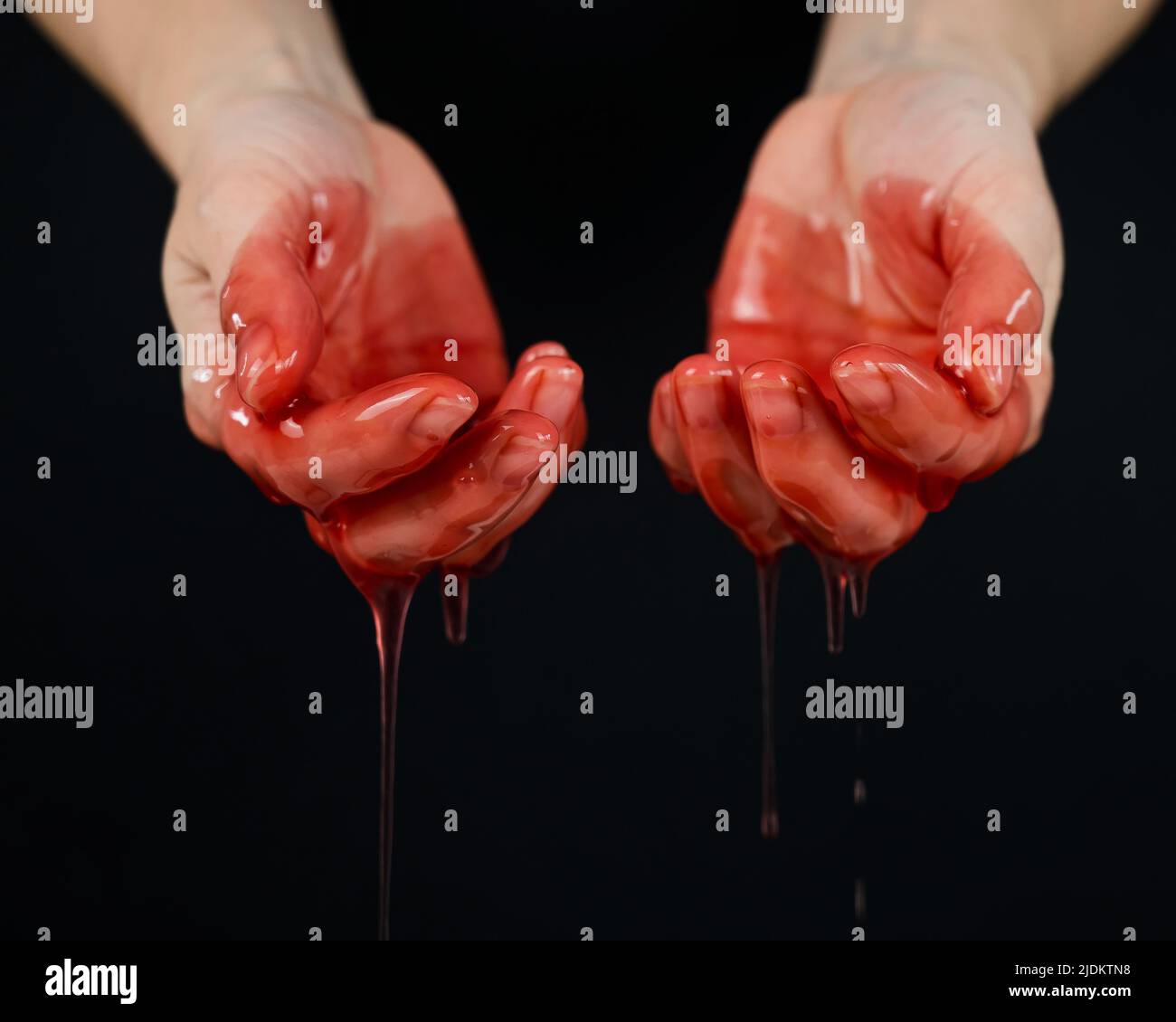 Frauenhände in einer zähflüssigen roten Flüssigkeit ähnlich dem Blut. Stockfoto