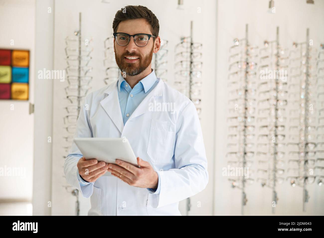 Schöner Augenarzt mit digitalem Tablet vor der Vitrine mit Brille Stockfoto