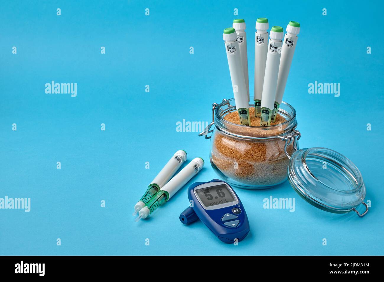 Insulinspritzenstifte stecken in einem Glas braunen Rohrzuckers und einem Blutzuckermessgerät auf blauem Hintergrund. Diabetes-Patientenbehandlung und Lifestyle-Konzept Stockfoto