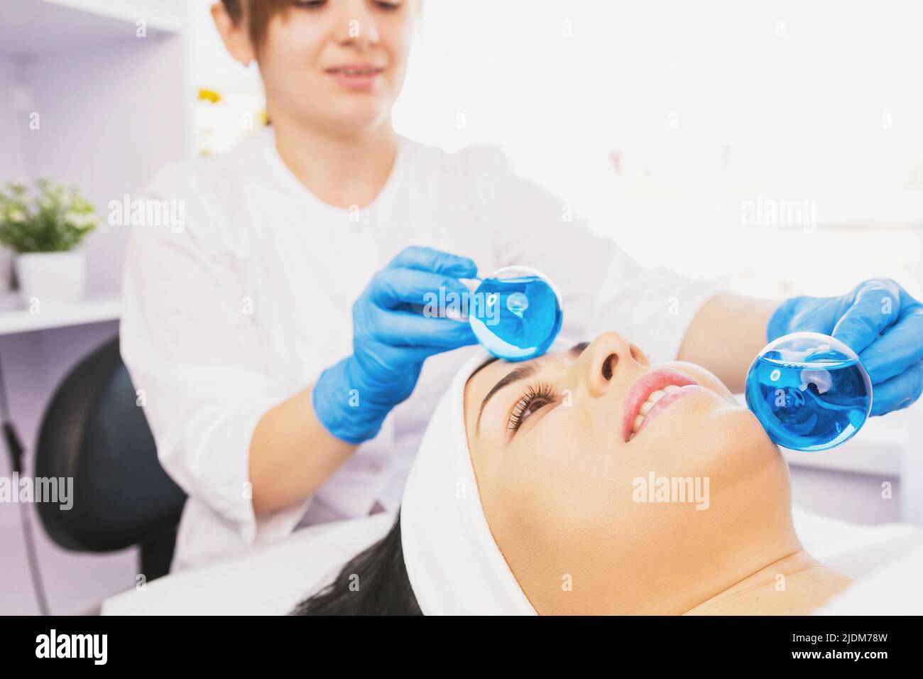 Zugeschnittenes Foto einer professionellen Fachfrau bei einer Gesichtsmassage mit eiskalter Kugel. Anti Falten Verjüngung Verfahren Stockfoto