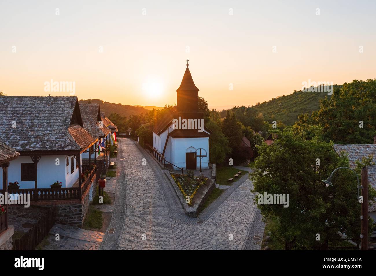 Herrlicher Sonnenuntergang über der katholischen Kirche im alten Dorf Hollókő. Dieses Dorf wurde zum UNESCO-Weltkulturerbe erklärt. Berühmtes Touristenziel. Stockfoto