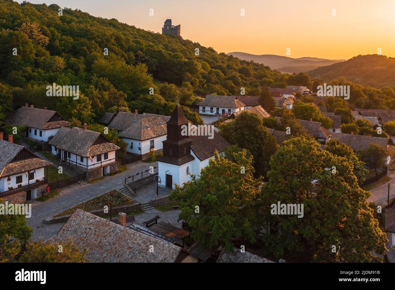 Luftaufnahme über ein winziges Dorf namens Hollókő mit spektakulärem Sommeruntergang über den Bergen von Cserhát. Berühmtes Touristenziel, UNESCO Welterbe Stockfoto