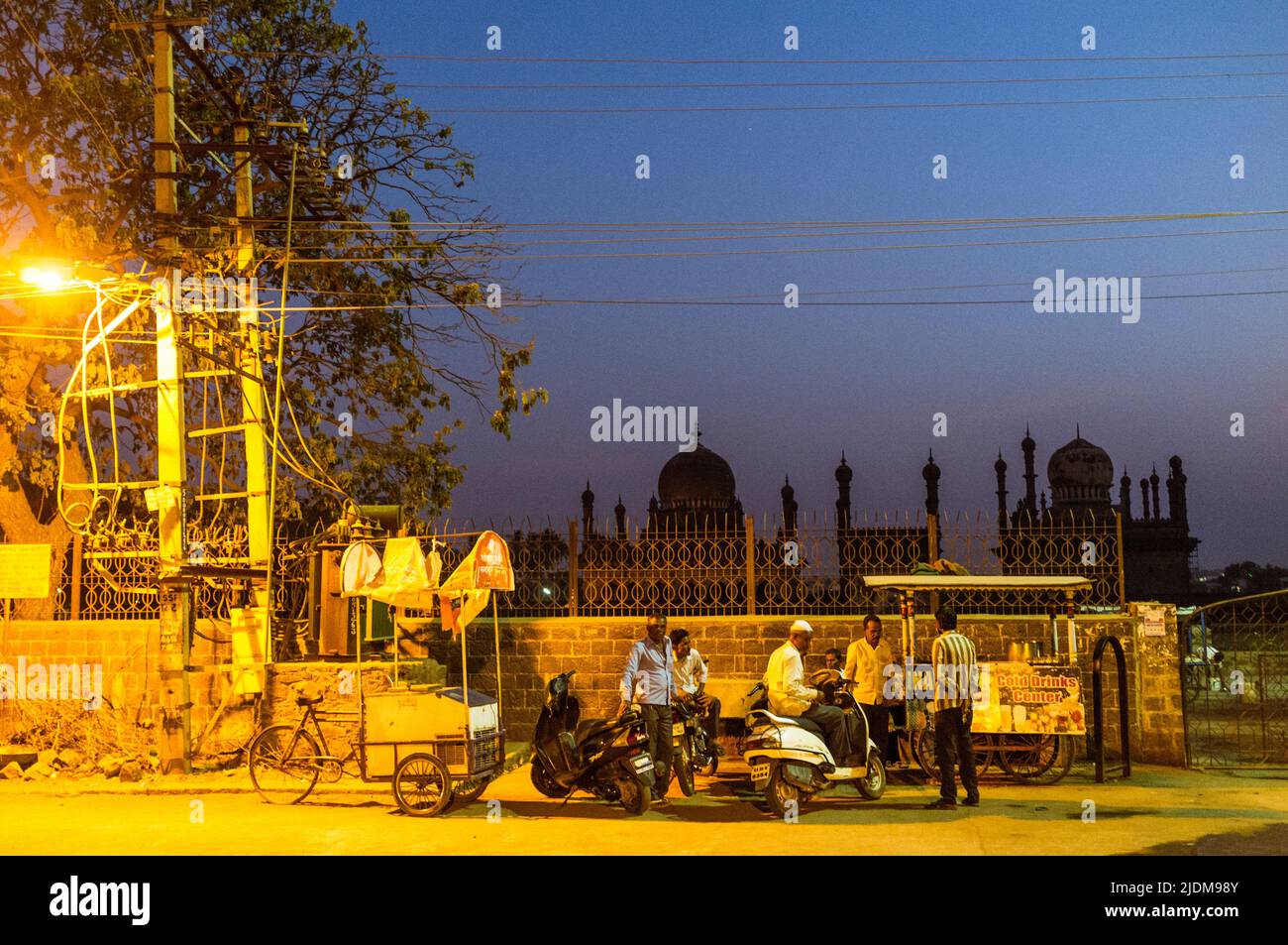 Bijapur, Karnataka, Indien : Eine Gruppe von Männern versammelt sich nachts um einen Stand mit kalten Getränken vor dem Ibrahim Rouza Mausoleum. Stockfoto
