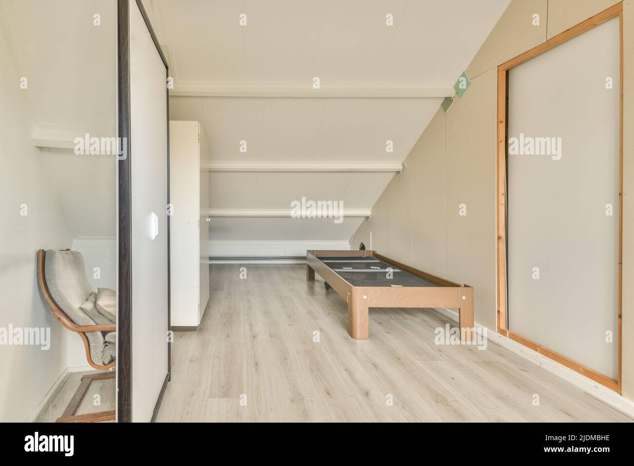 Minimalistisches, helles Zimmer im Dachgeschoss mit Bett, komfortablem Arbeitsplatz und Parkett Stockfoto