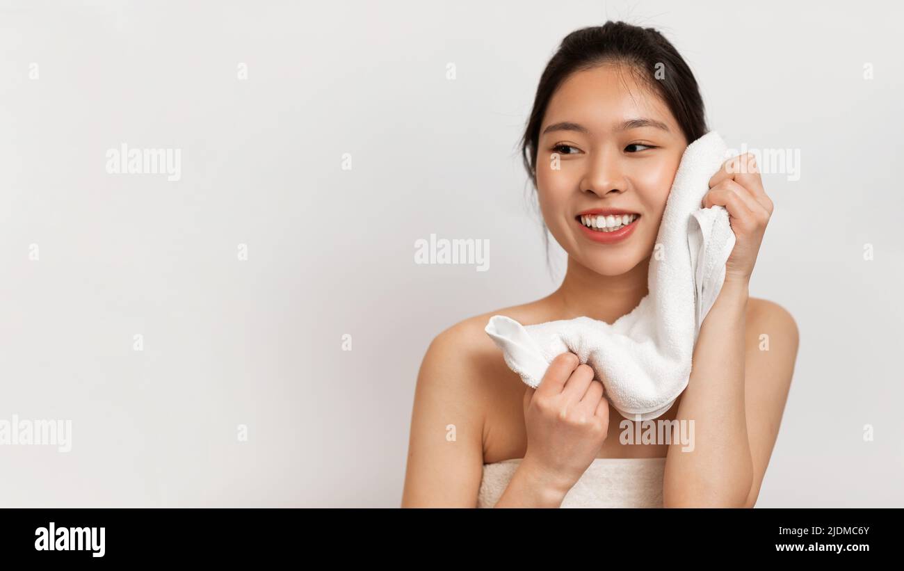 Happy Beautiful Asian Lady Trocknen Gesicht mit weichem Handtuch zur Seite schauen, posiert über weißen Studio-Hintergrund, freien Raum Stockfoto