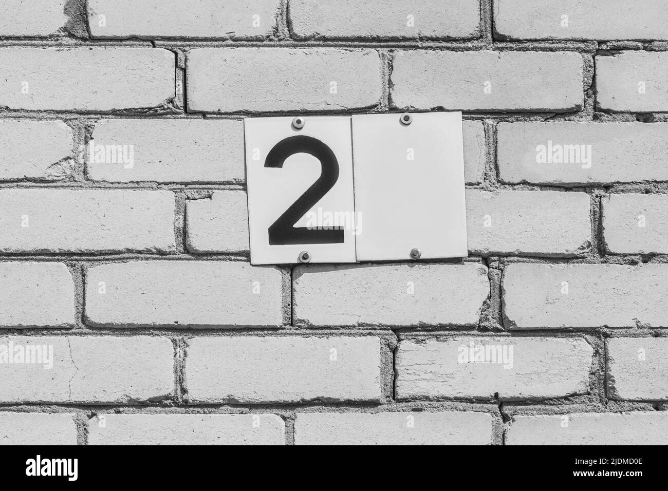 Nummer 2 Zeichen Symbol Ziffer Adressennummerierung auf der weißen Backsteinmauer des Hauses außen, Nahaufnahme. Stockfoto