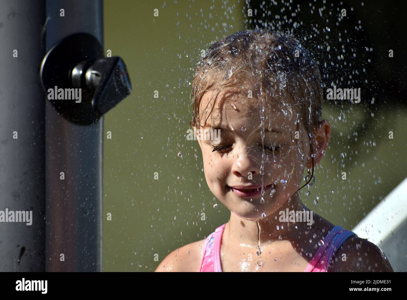 Das Kind kühlt sich während des heißen Wetters im Sommer unter einer Außendusche ab Stockfoto