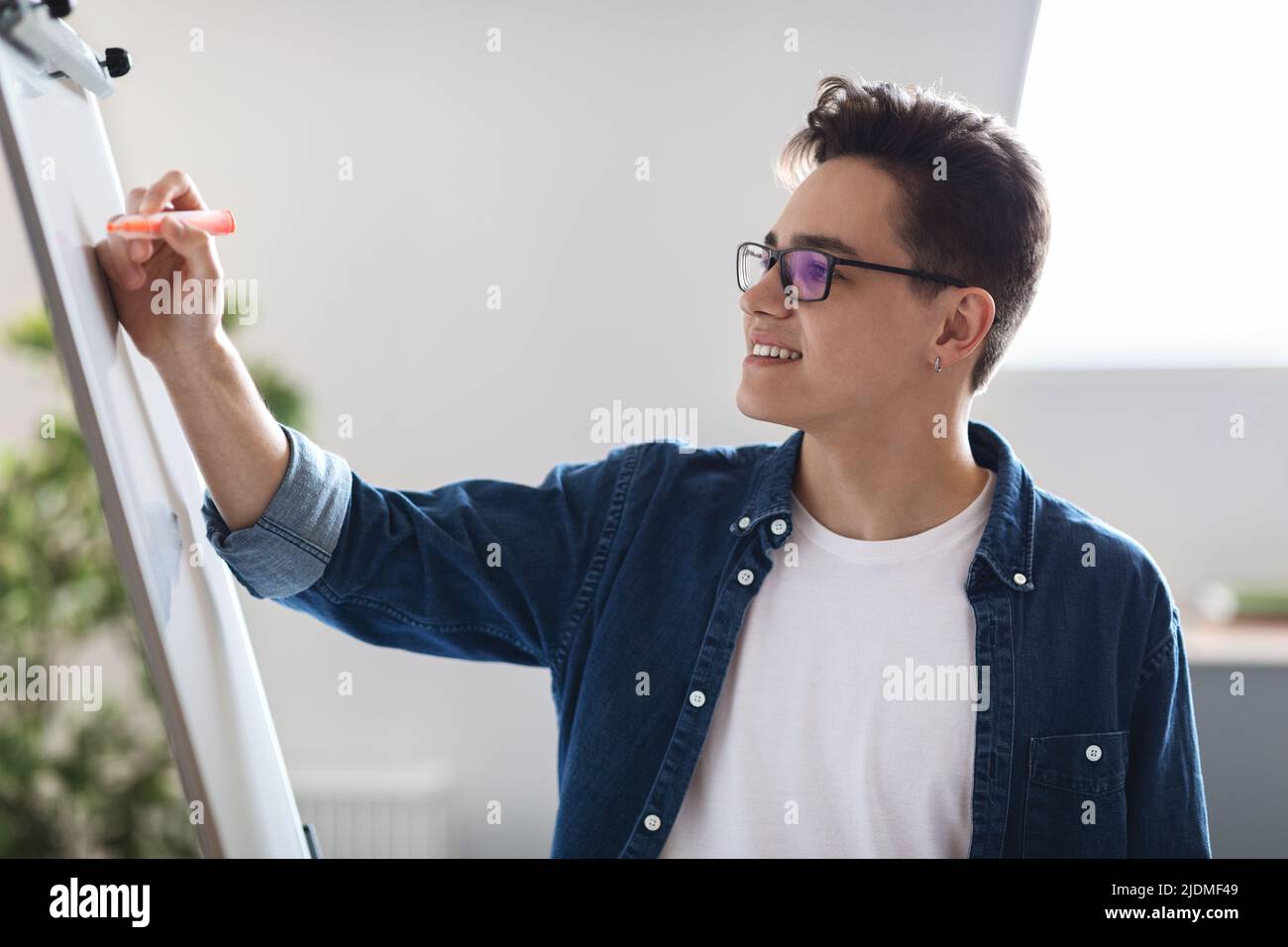 Lächelnder junger männlicher Unternehmer, der im Büro Notizen auf das Whiteboard schreibt Stockfoto