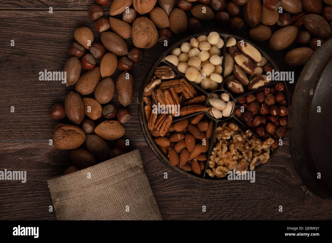 Gemischte Nüsse in einem alten Gewürzdose-Behälter und einem hessischen Beutel aus nächster Nähe auf dunklem Holzhintergrund Stockfoto