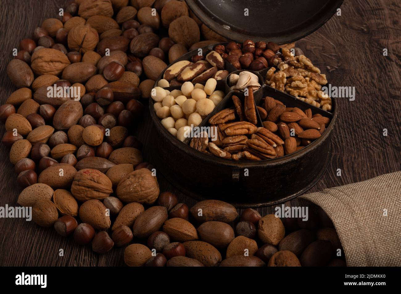 Gemischte Nüsse in einem alten Gewürzdose-Behälter und einem hessischen Beutel aus nächster Nähe auf dunklem Holzhintergrund Stockfoto