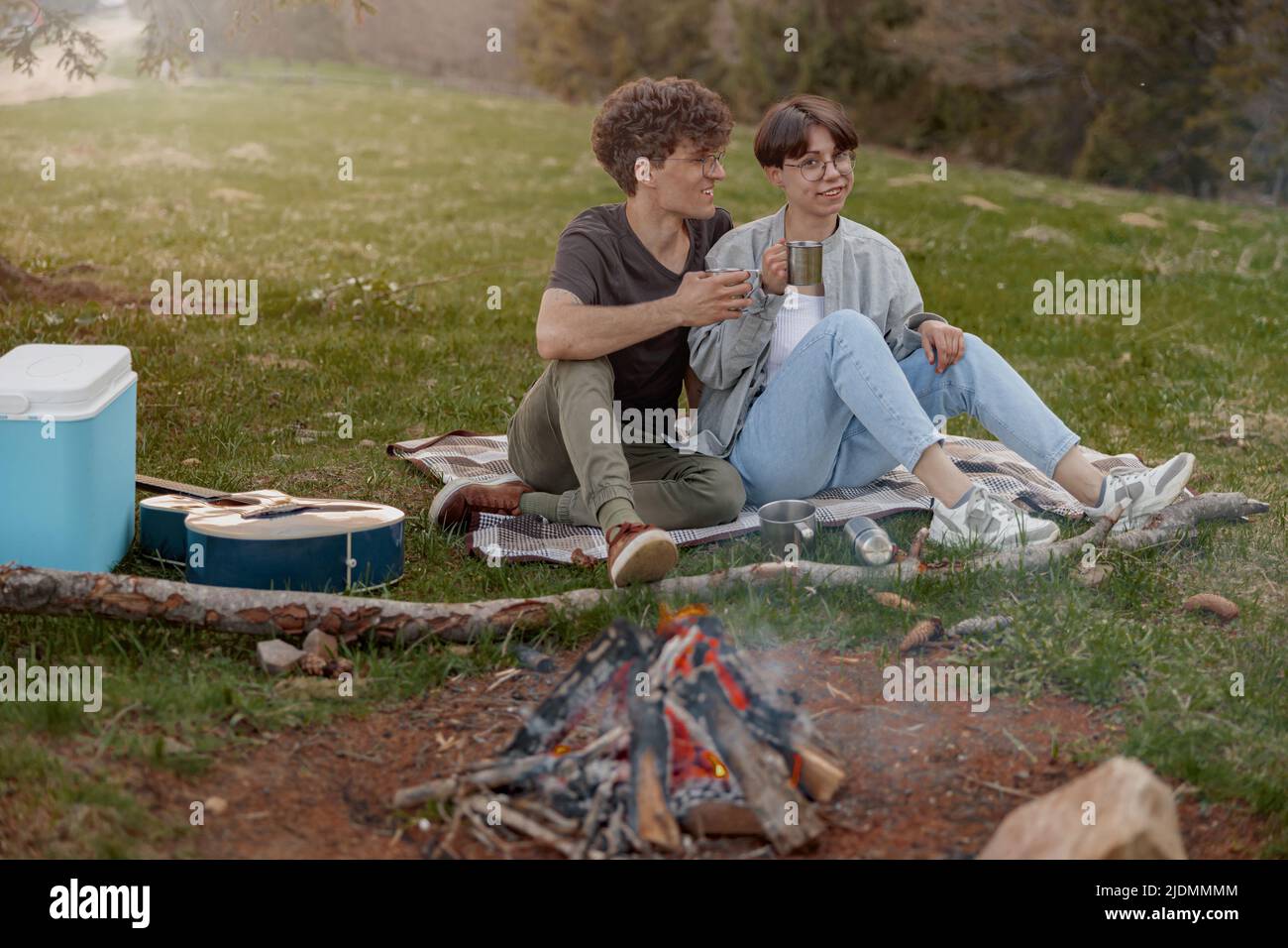 Fröhliches Paar sitzt auf Gras beim Picknick, redet und trinkt Tee oder Kaffee. Tourismus. Stockfoto