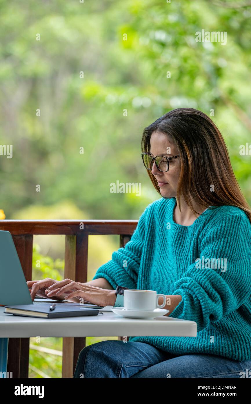 Junge Lateinamerikanerin, die in einem Café im Freien an ihrem Laptop arbeitet und dabei eine Tasse Kaffee trinkt, Panama, Mittelamerika Stockfoto