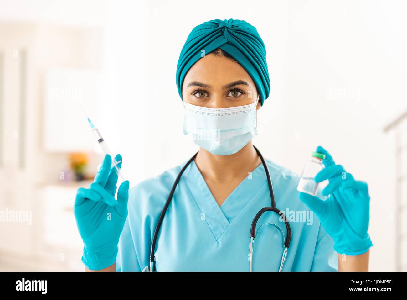 Portrait einer biracial jungen Ärztin in schützender Gesichtsmaske mit Spritze und Medizin in der Klinik Stockfoto