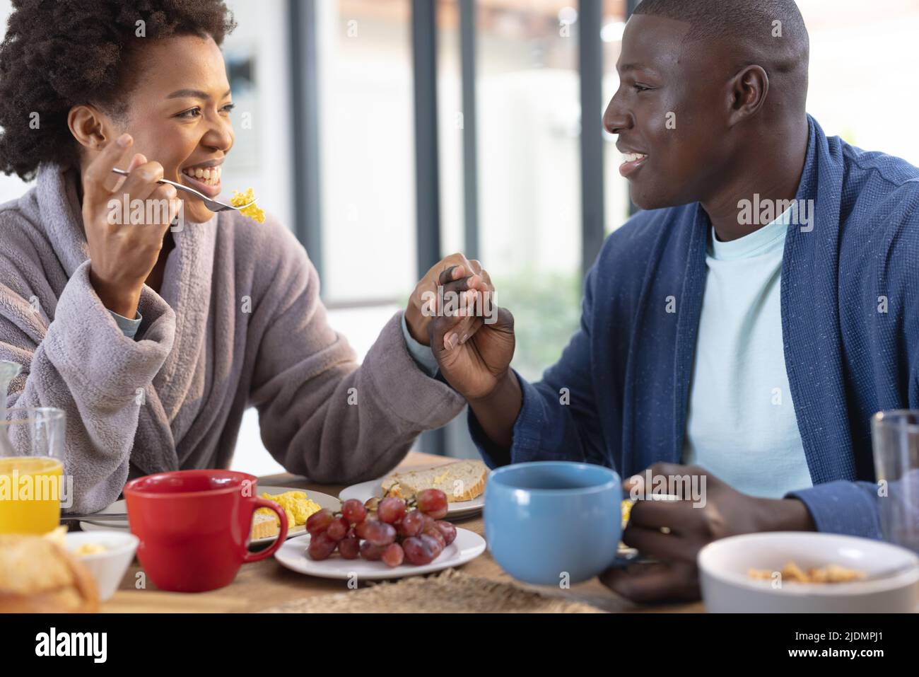 Romantisches afroamerikanisches Paar mittlerer Erwachsenen, das beim Frühstück am Esstisch die Hände hält Stockfoto