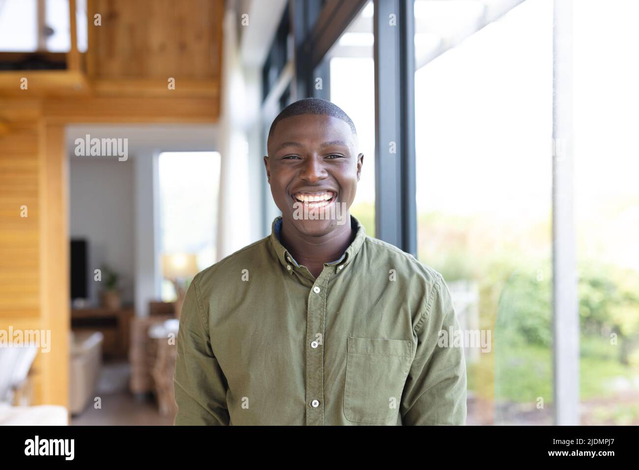 Porträt eines fröhlichen afroamerikanischen Mannes mit mittlerem Erwachsenenalter, der zu Hause am Fenster steht und lacht Stockfoto