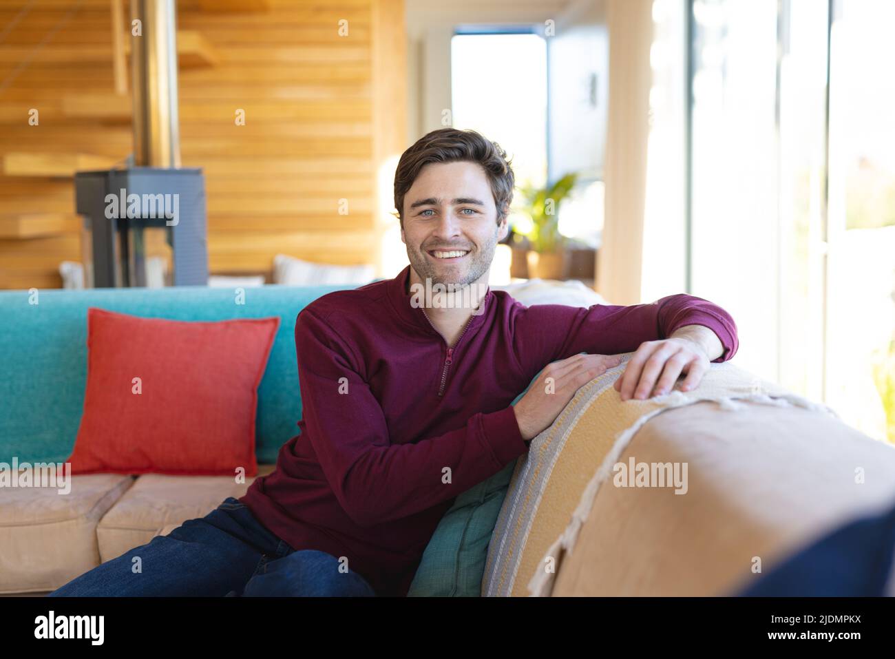 Porträt eines lächelnden, hübschen kaukasischen jungen Mannes, der im Wohnzimmer auf dem Sofa sitzt Stockfoto