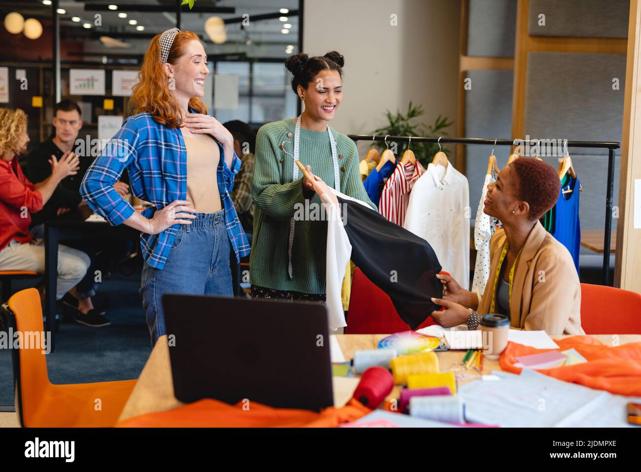 Lächelnde Biracial weibliche Modedesignerin zeigt Kleidungsstücke an Kollegen im Studio Stockfoto