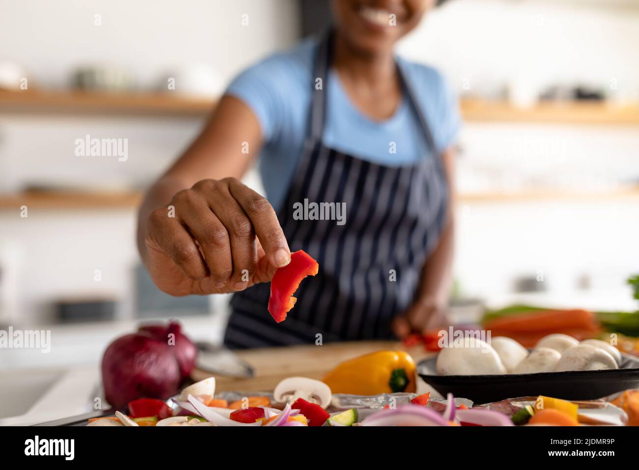 Mittelteil der Birazialfrau, die die Paprikascheibe hält, während sie in der Küche zu Hause Essen macht Stockfoto