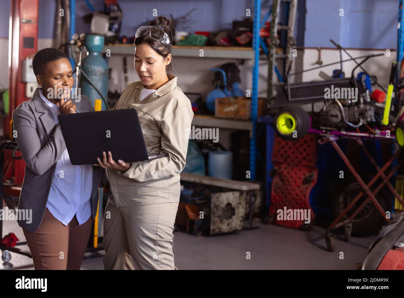 Schweißerinnen mit mittleren Erwachsenen und verschiedenen Rassen diskutieren während der Arbeit in der Werkstatt über die Arbeit am Laptop Stockfoto