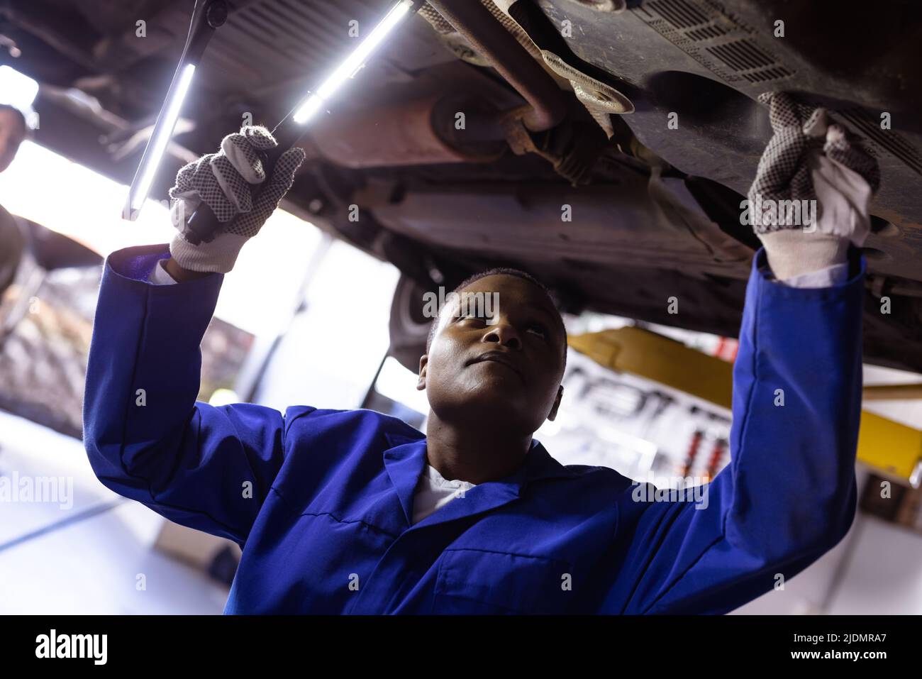 afroamerikanische Mechanikerin mit mittlerem Erwachsenen, die Beleuchtungsausrüstung verwendet, während sie das Auto überprüft Stockfoto