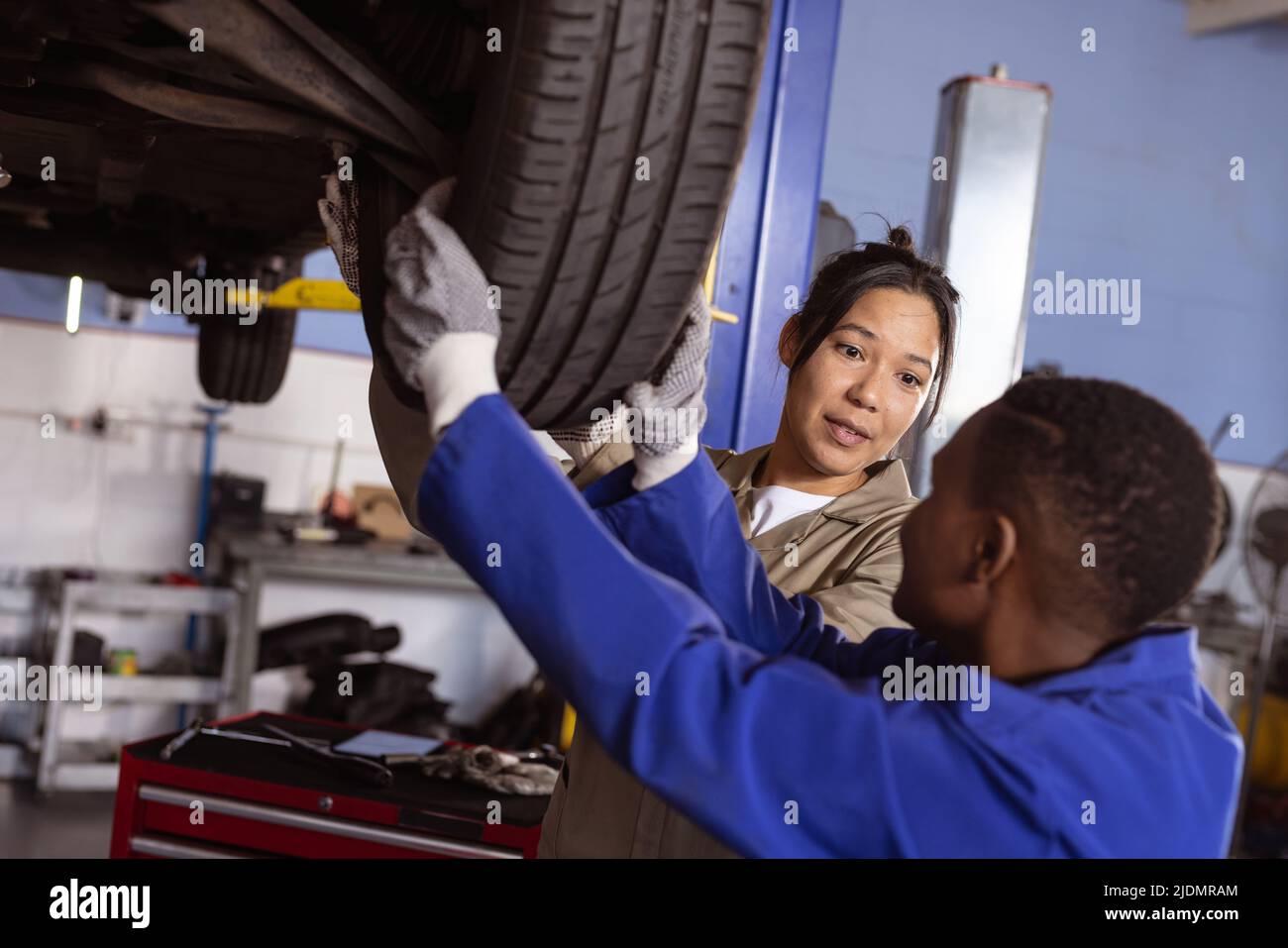 Multirassische Technikerinnen mittlerer Erwachsener, die den Autoreifen untersuchen, während sie ihn in der Werkstatt reparieren Stockfoto