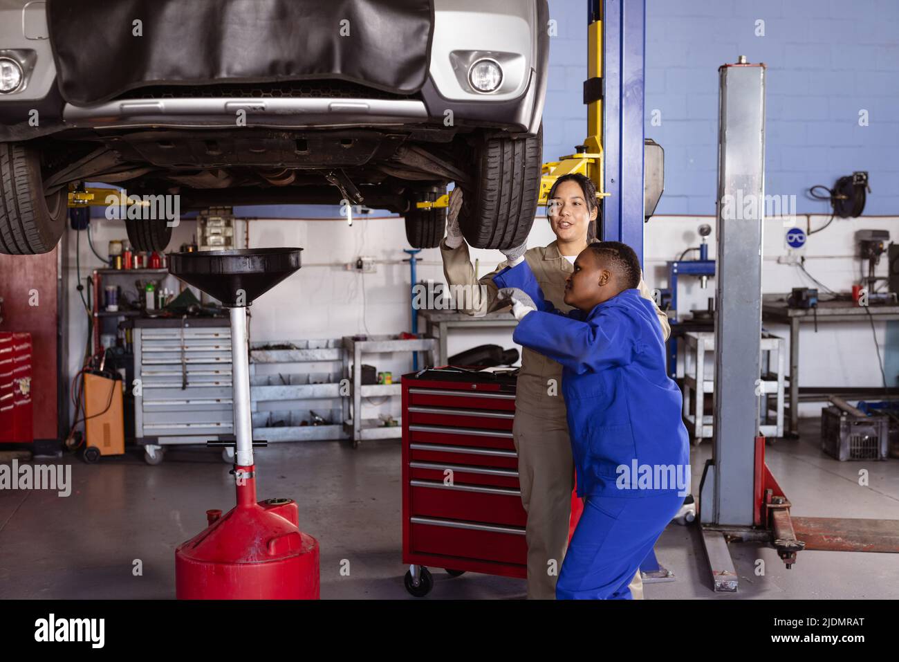 Multirassische Ingenieure mit mittlerem Erwachsenenalter, die zusammen in der Werkstatt ein Auto auf dem Autoaufzug reparieren Stockfoto