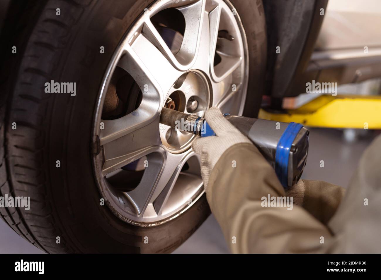 Zugeschnittenes Bild einer weiblichen asiatischen Mechanikerin mit mittlerem Erwachsenen, die ein Arbeitswerkzeug verwendet, während sie den Autoreifen repariert Stockfoto