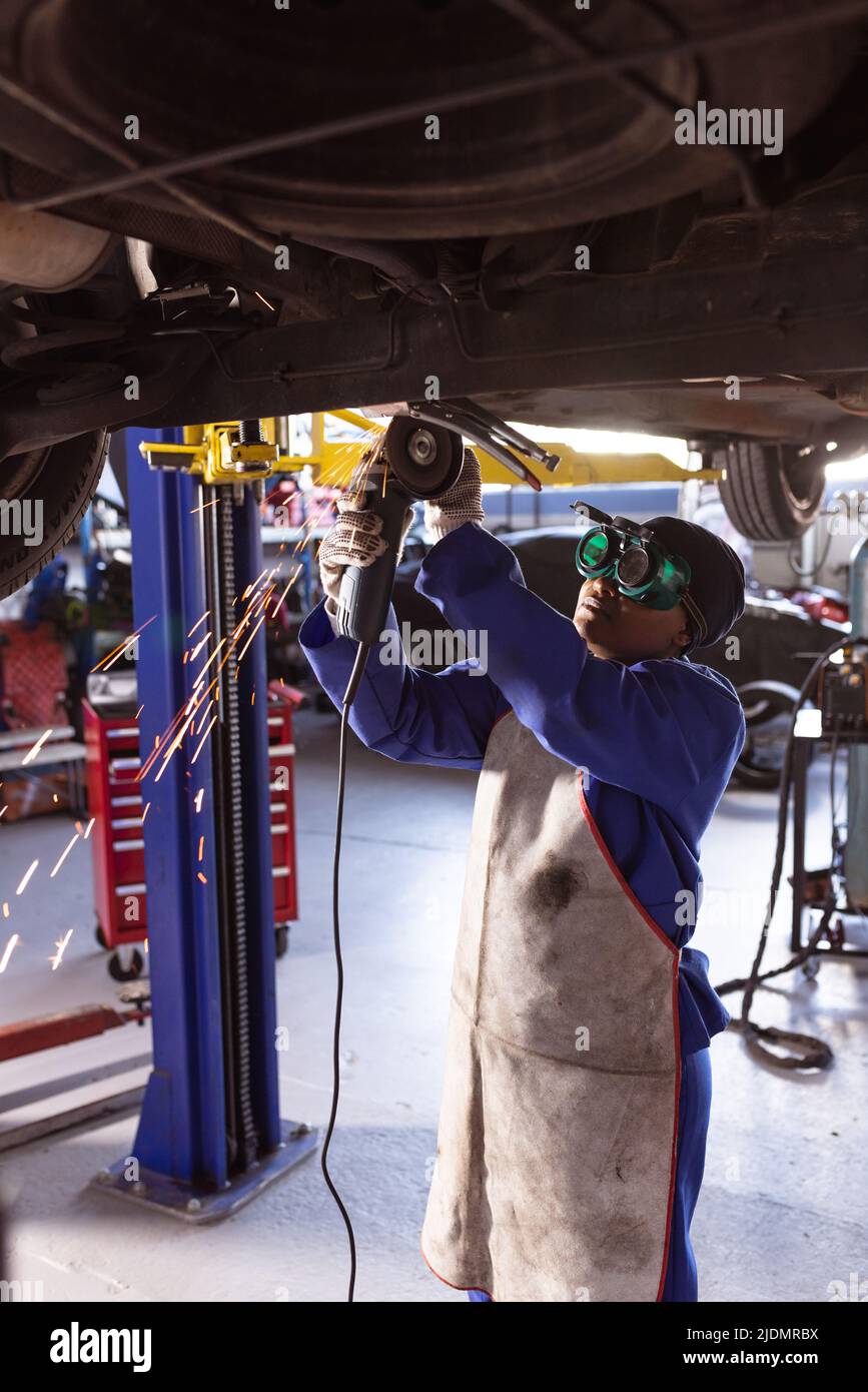 afroamerikanische Schweißerin mit mittlerem Erwachsenenalter, die während der Reparatur des Autos eine schützende Arbeitskleidung trägt Stockfoto