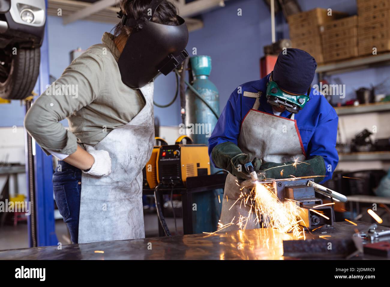 Weibliche Schweißerinnen mit mittlerer Erwachsene, die während der Arbeit in der Werkstatt eine schützende Arbeitskleidung tragen Stockfoto