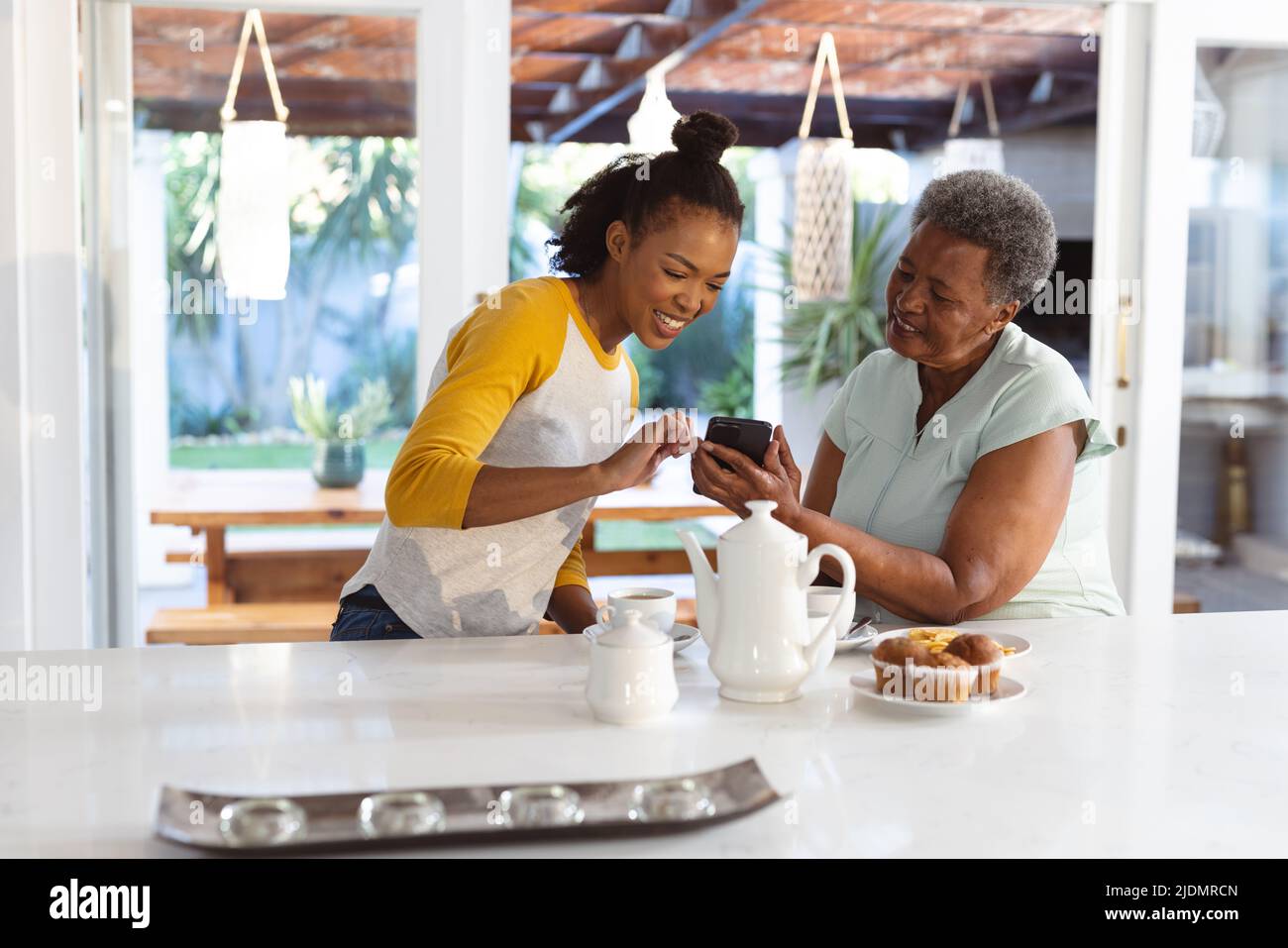 afroamerikanische ältere Frau, die der glücklichen Tochter ein Smartphone zeigt, während sie Kaffee und Cupcakes getrunken hat Stockfoto