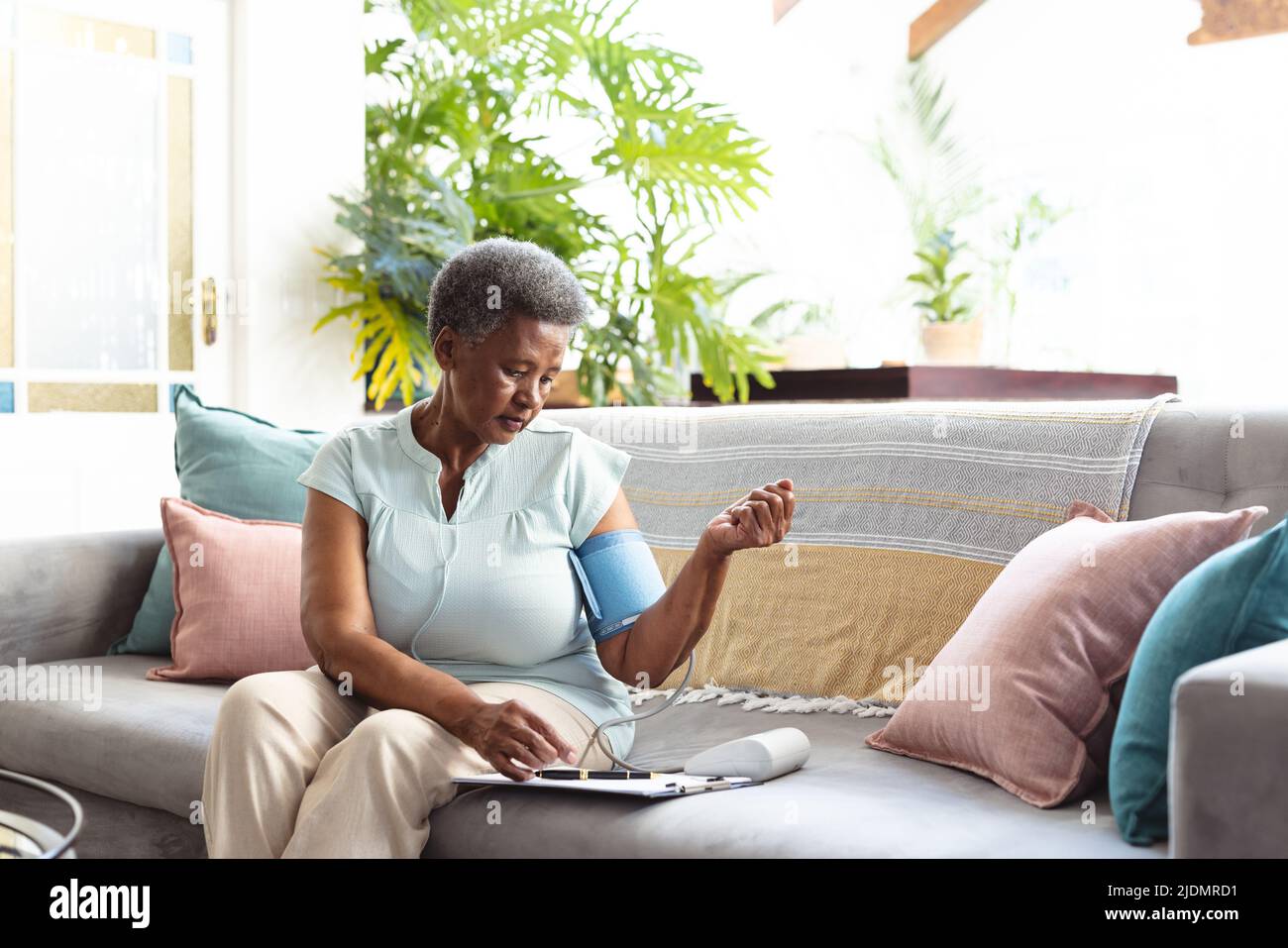 afroamerikanische ältere Frau mit medizinischen Berichten auf dem Sofa, die den Blutdruck mit einem Messgerät untersuchen Stockfoto