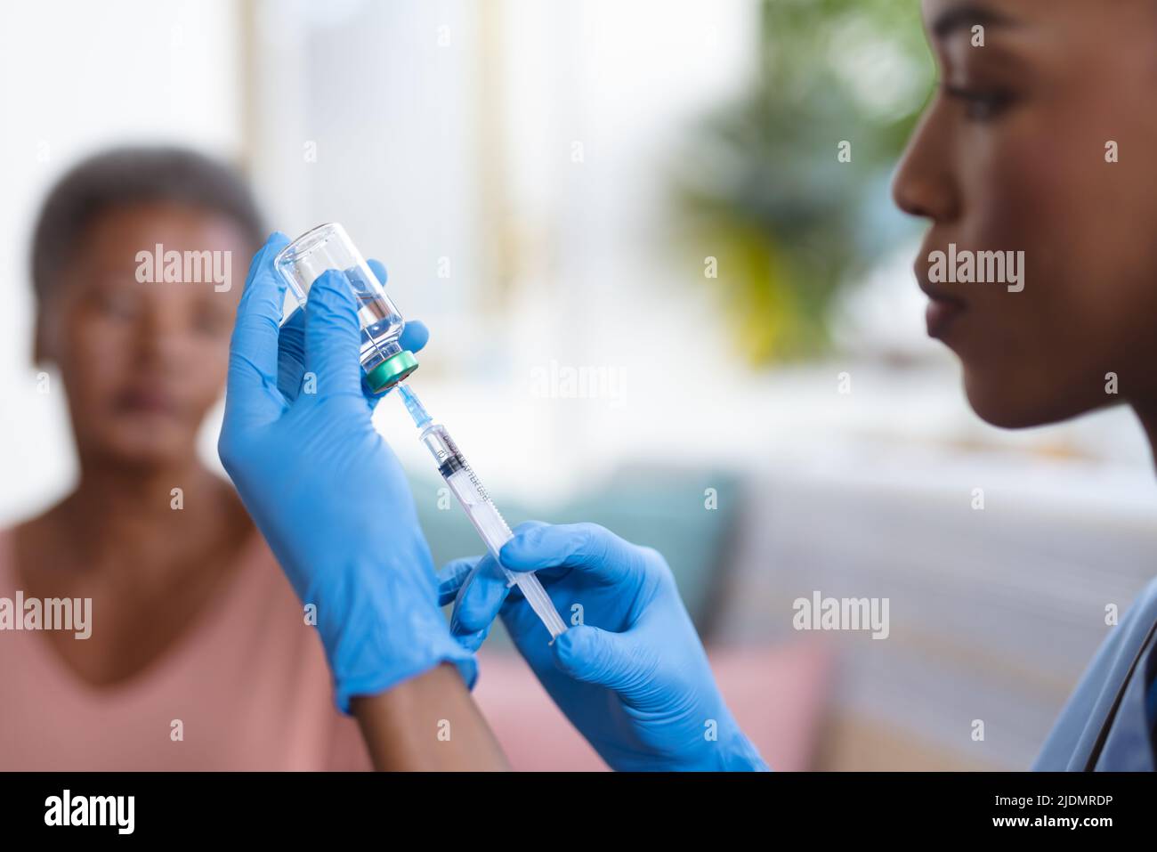 afroamerikanische ältere Frau, die eine junge Ärztin ansieht, die zu Hause Fläschchen und Spritze hält Stockfoto