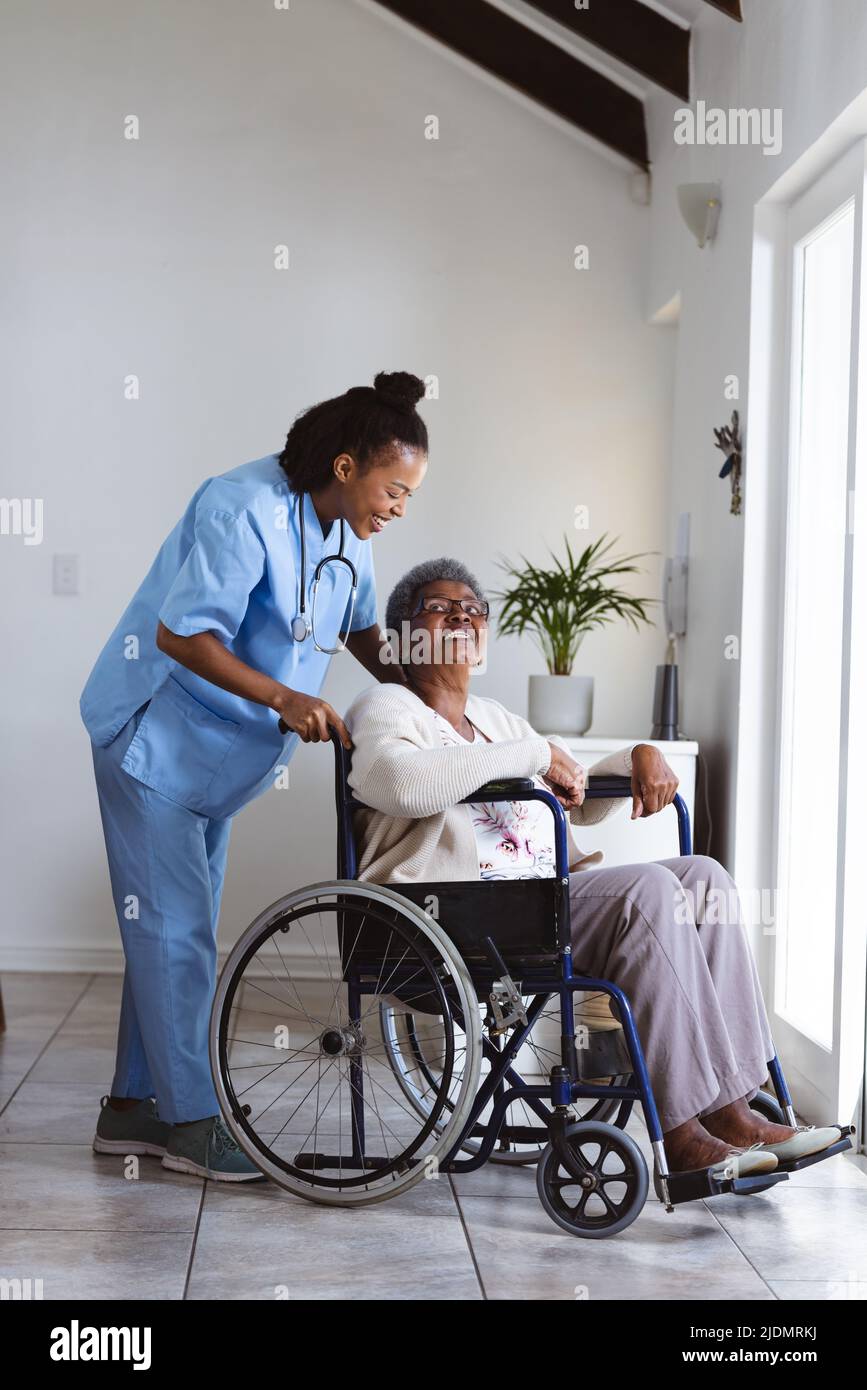 Lächelnde afroamerikanische Ärztin, die zu Hause eine ältere Frau im Rollstuhl hält Stockfoto