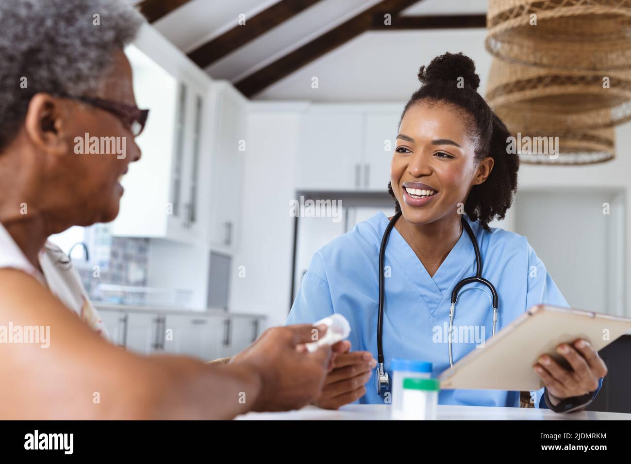 Lächelnder afroamerikanischer Arzt mit digitalem pc, der zu Hause älteren Patienten Medikamente gibt Stockfoto