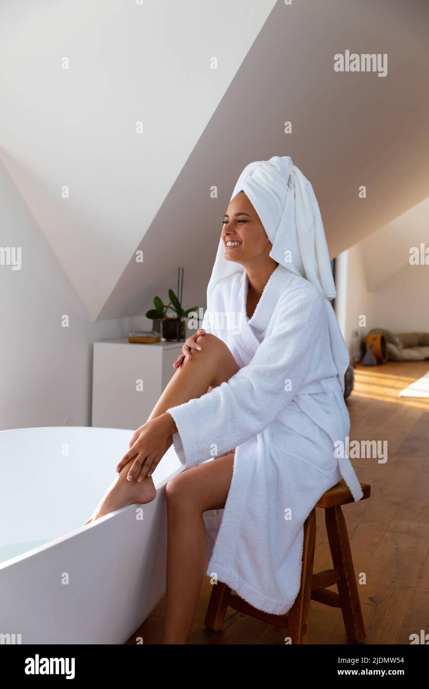 Lächelnde junge kaukasische Frau streichelt ihr Bein im Badezimmer zu Hause, Platz kopieren Stockfoto